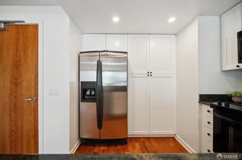 a view of a refrigerator in kitchen and an empty room with wooden floor