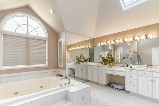 a large white bathroom with a large tub a double vanity sink a vanity and a large window