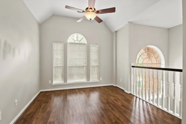 an empty room with wooden floor fan and windows