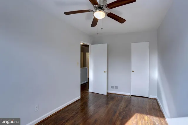 an empty room with wooden floor ceiling fan and windows