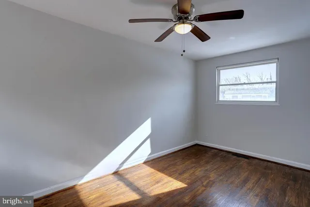 an empty room with wooden floor ceiling fan and windows