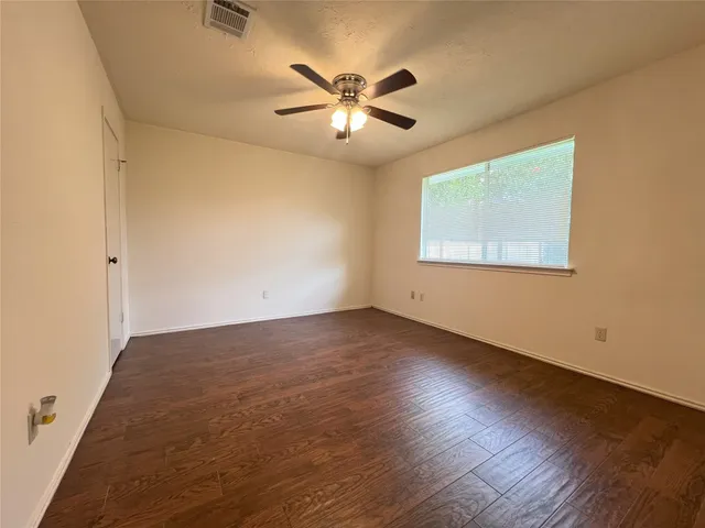 an empty room with wooden floor fan and windows