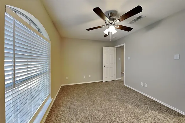 a view of an empty room with wooden floor and a ceiling fan