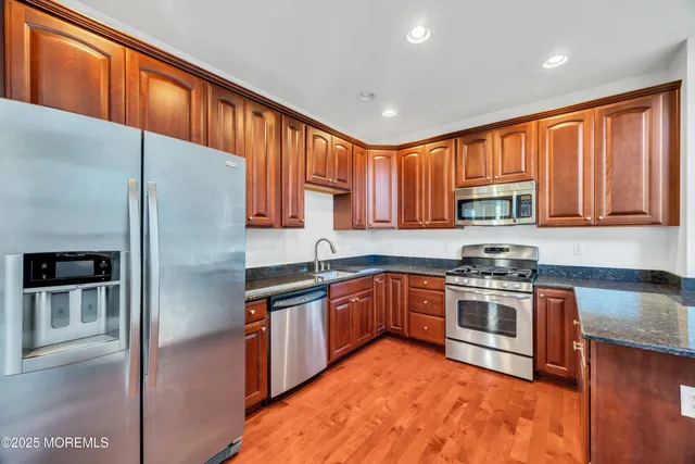 a kitchen with stainless steel appliances granite countertop a stove a sink dishwasher a refrigerator and cabinets with wooden floor