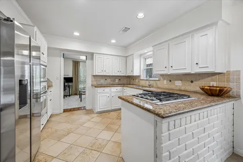 a kitchen with stainless steel appliances granite countertop a stove a refrigerator a sink and white cabinets