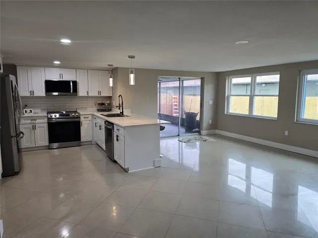 a large kitchen with stainless steel appliances granite countertop a stove top oven a sink dishwasher and white cabinets with wooden floor