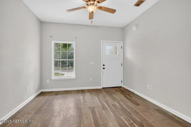 an empty room with wooden floor chandelier fan and windows
