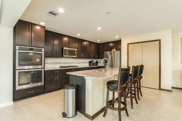 a kitchen with stainless steel appliances kitchen island granite countertop a stove a sink a refrigerator with grey cabinets and wooden floor