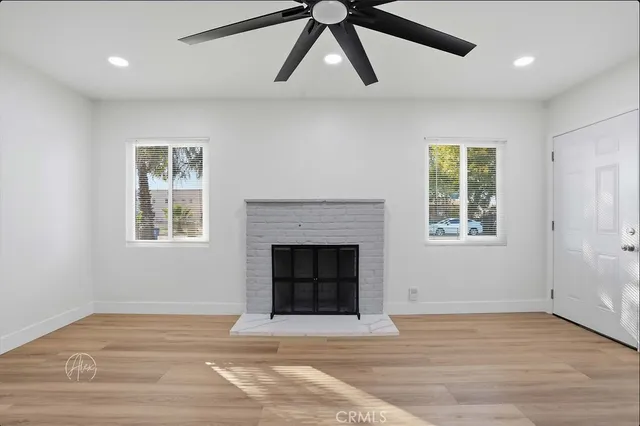 an empty room with wooden floor a ceiling fan a fireplace and windows