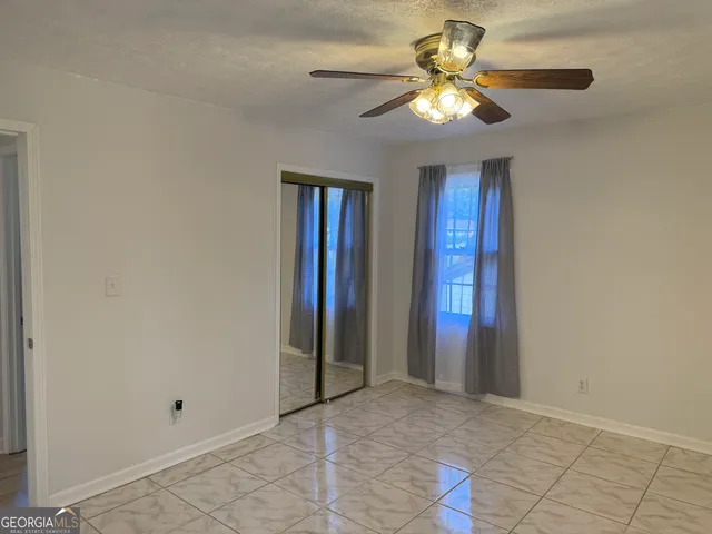 a view of an empty room with window and chandelier fan