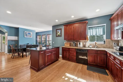 a kitchen with stainless steel appliances granite countertop wooden cabinets a sink a stove a dining table and chairs