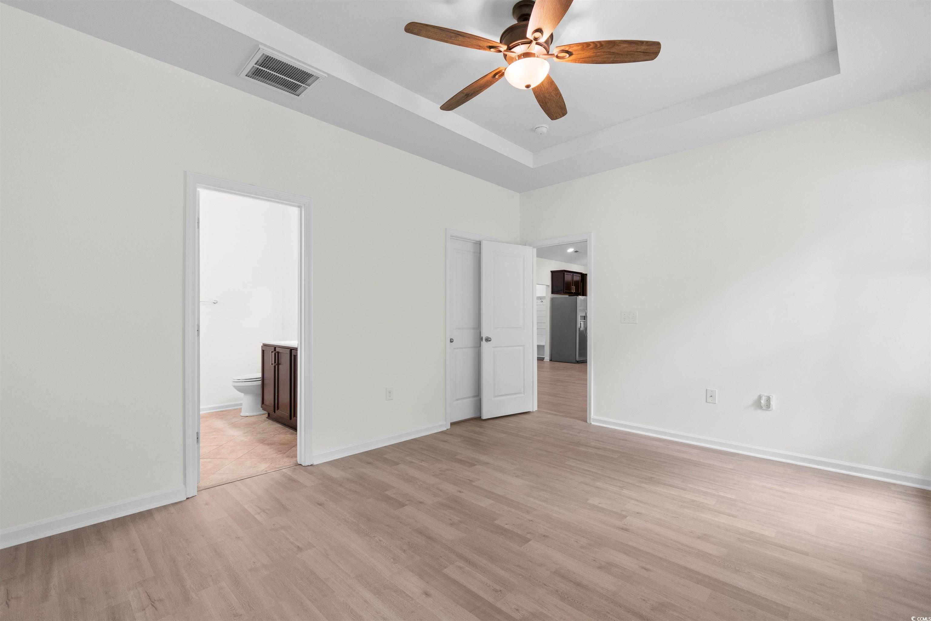 124 Shady Arbor Loop Longs, SC 29568 - Photo 16 of 40 Unfurnished bedroom featuring light wood-type flooring, stainless steel refrigerator with ice dispenser, a tray ceiling, ensuite bathroom, and ceiling fan