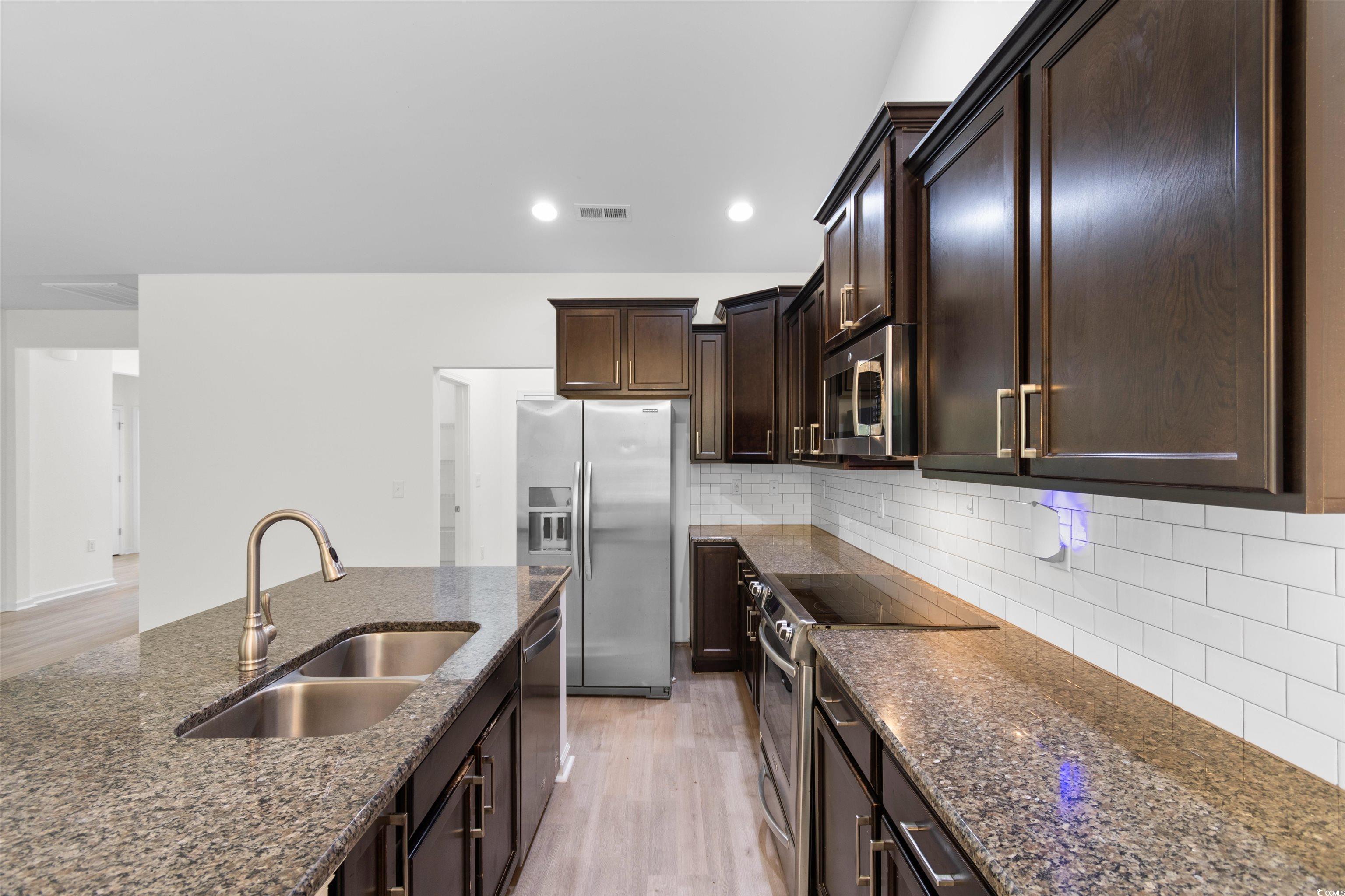 124 Shady Arbor Loop Longs, SC 29568 - Photo 6 of 40 Kitchen with appliances with stainless steel finishes, dark stone countertops, light wood finished floors, dark brown cabinetry, and decorative backsplash
