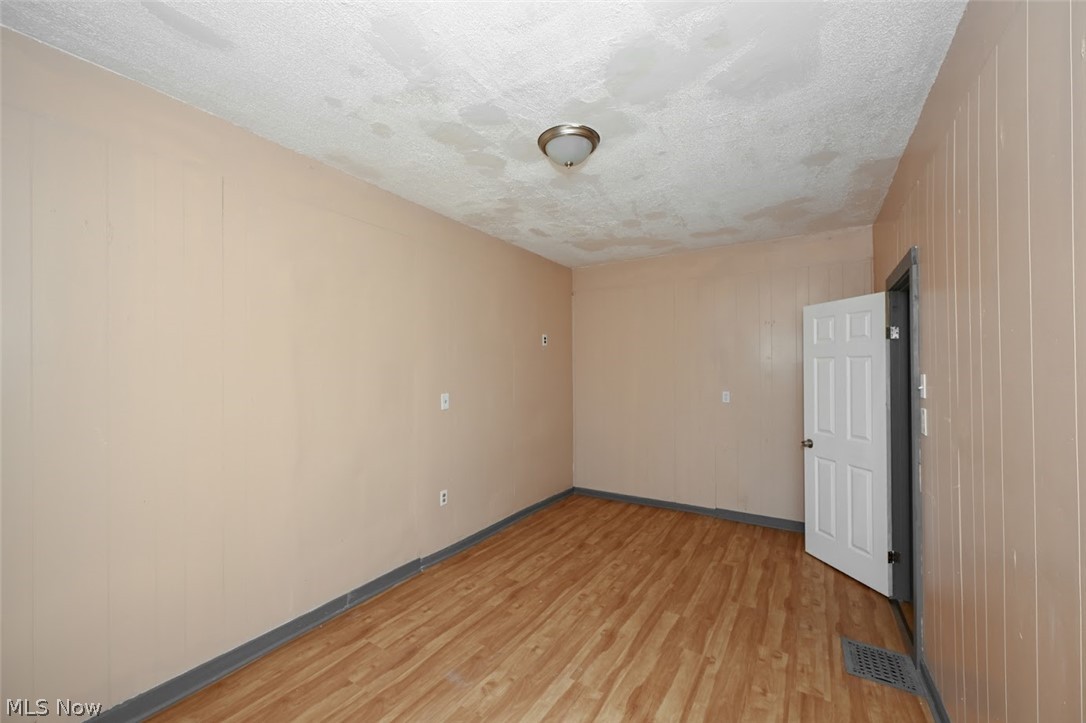 868 North Main Street Akron, OH 44310 - Photo 7 of 30 Spare room featuring a textured ceiling, light wood-style floors, and wood walls