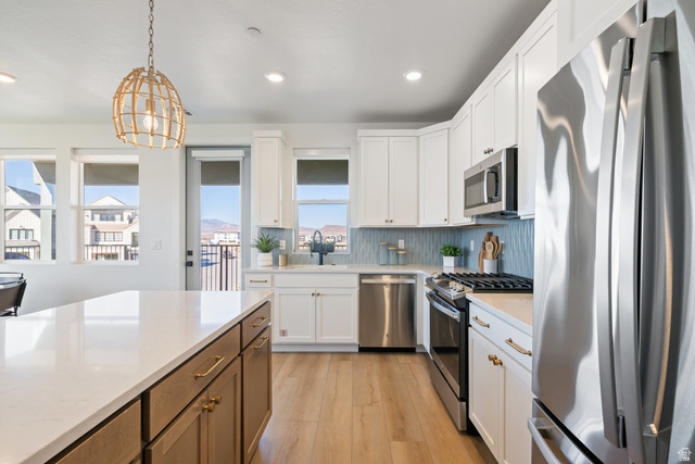 762 West Periwinkle Lane, Unit 102 St. George, UT 84790 - Photo 4 of 40 Two tone kitchen with stainless steel appliances, light wood-type flooring, decorative light fixtures, dual tone cabinets, and light stone counters