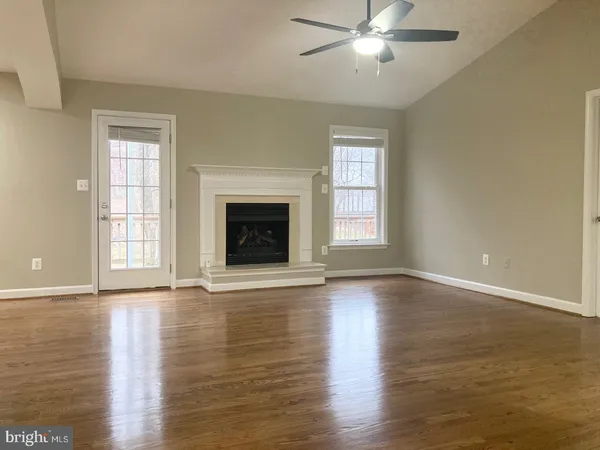 a view of an empty room with wooden floor fireplace and a window