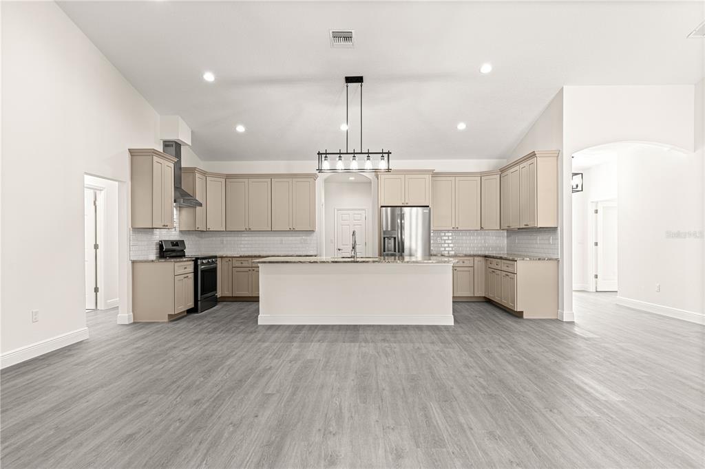 12411 Southwest 71st Lane Road Ocala, FL 34481 - Photo 11 of 50 a large kitchen with kitchen island a stove a sink dishwasher a refrigerator and white cabinets with wooden floor