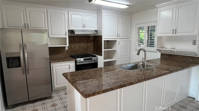 a kitchen with granite countertop a sink dishwasher a refrigerator and white cabinets