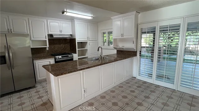 a kitchen with granite countertop a sink a counter top space cabinets stainless steel appliances and a window