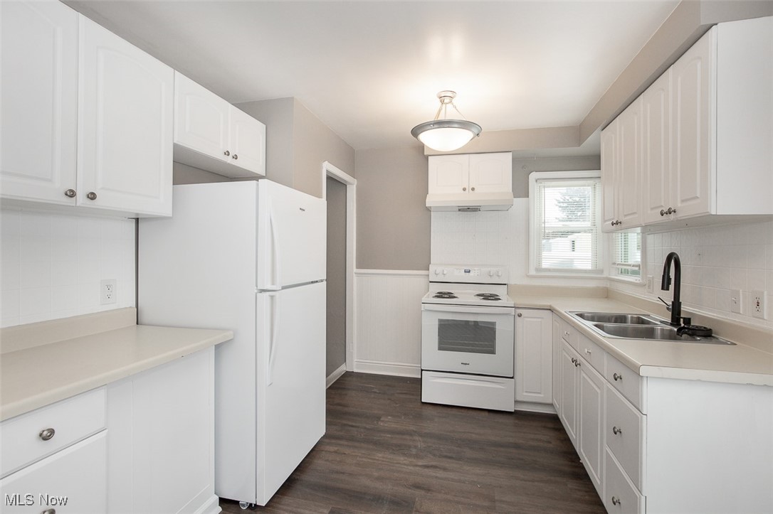 12328 Granger Road Cleveland, OH 44125 - Photo 17 of 37 Kitchen featuring white appliances, light countertops, decorative backsplash, dark wood-type flooring, and a wainscoted wall