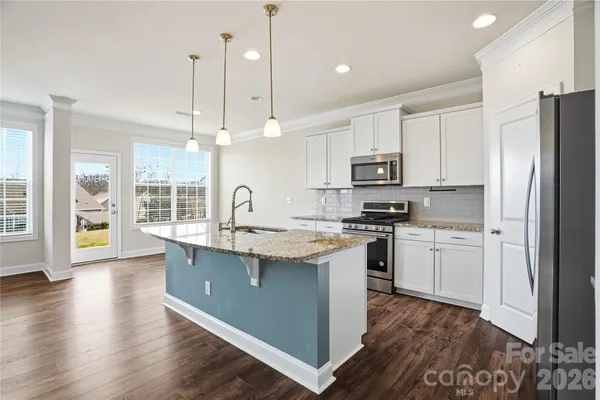 a kitchen with stainless steel appliances granite countertop a sink a stove a refrigerator and island with wooden floor