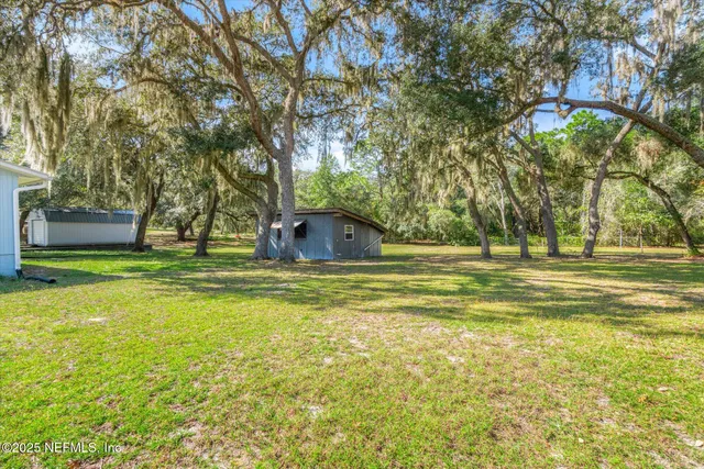 a view of a white house with a small yard and large tree
