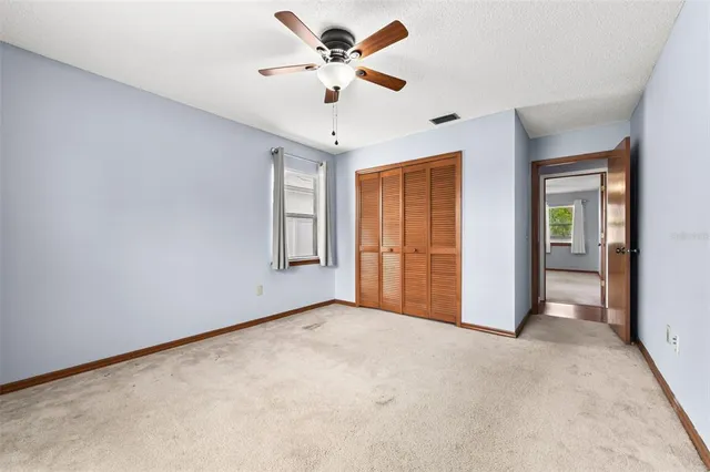an empty room with chandelier fan and windows