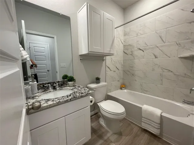 a bathroom with a granite countertop bathtub shower sink mirror vanity and toilet