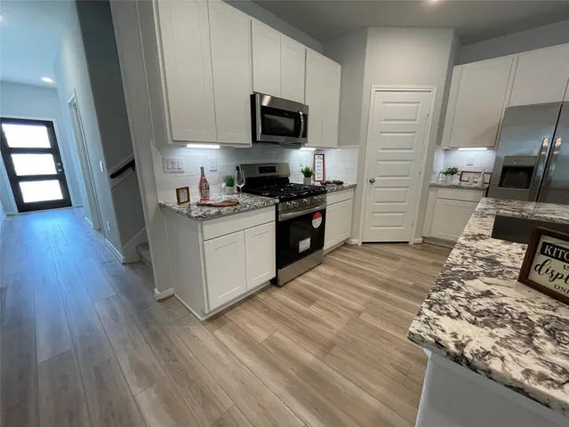 a kitchen with granite countertop a stove top oven a sink dishwasher and a refrigerator with wooden floor