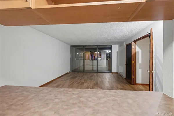 a view of an empty room with wooden floor kitchen and a window