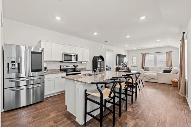 a kitchen with stainless steel appliances kitchen island granite countertop a stove a sink a refrigerator and white cabinets with wooden floor