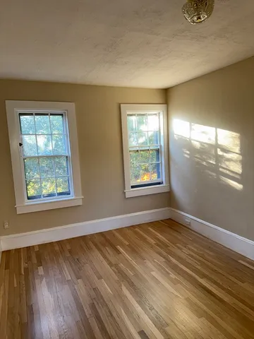 a view of an empty room with window and wooden floor