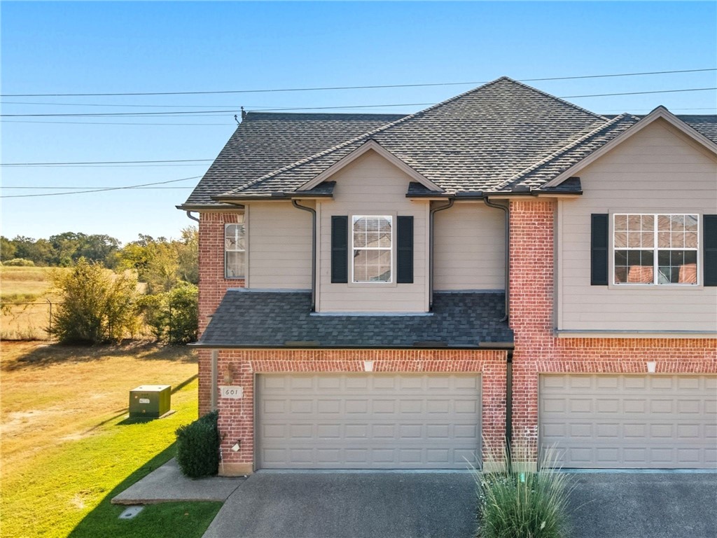 View of front of property featuring driveway, a shingled roof, a garage, and brick siding