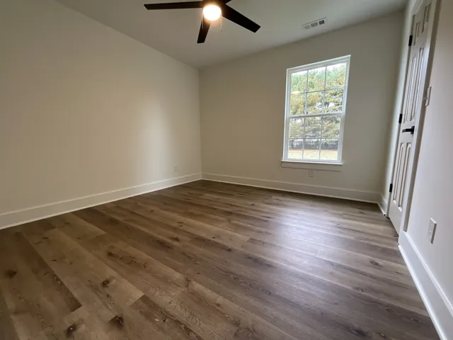 an empty room with wooden floor chandelier fan and windows