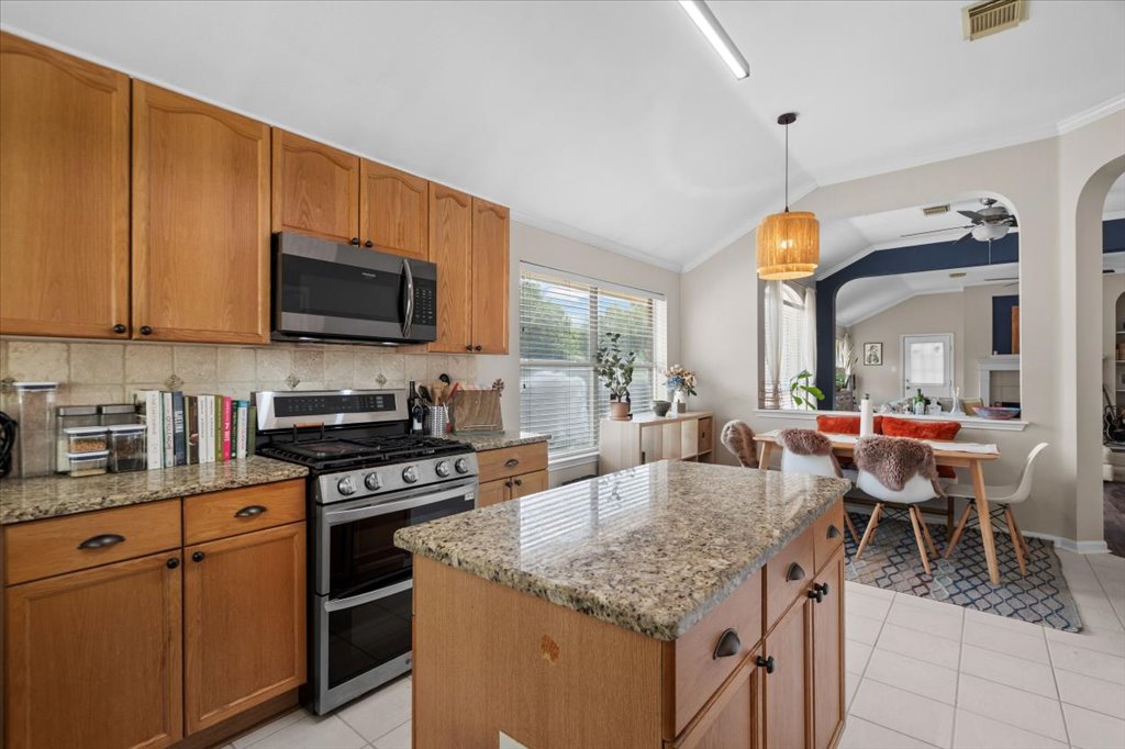 Warm wood cabinetry and granite countertops frame a central island in this vaulted-ceiling kitchen.