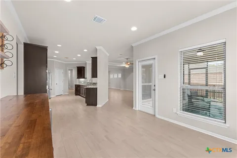 a view of an empty room with wooden floor and a kitchen