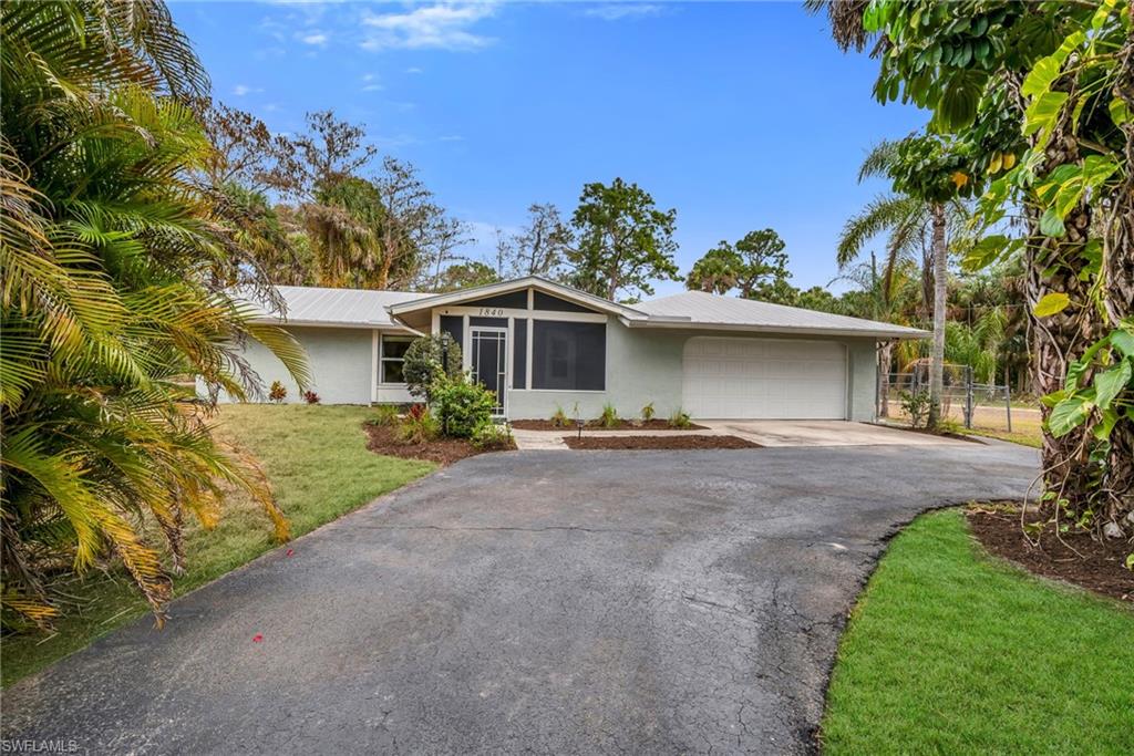 View of front of house featuring stucco siding, driveway, an attached garage, a front lawn, and a metal roof