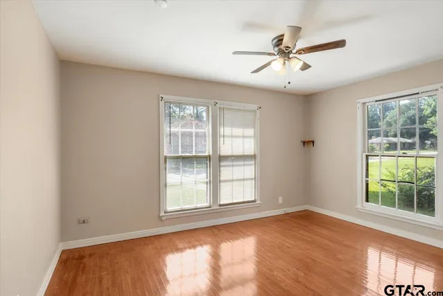 an empty room with wooden floor fan and windows