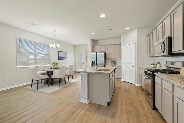 a kitchen with stainless steel appliances kitchen island granite countertop a stove top oven a sink a dining table and chairs with wooden floor