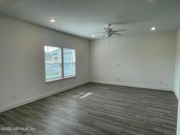 an empty room with wooden floor ceiling fan and windows