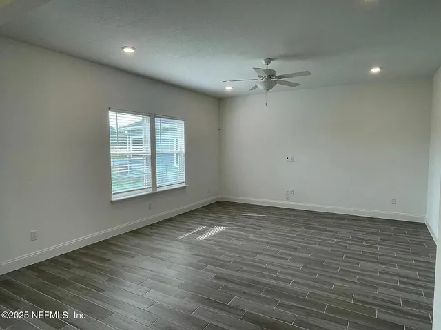 an empty room with wooden floor ceiling fan and windows