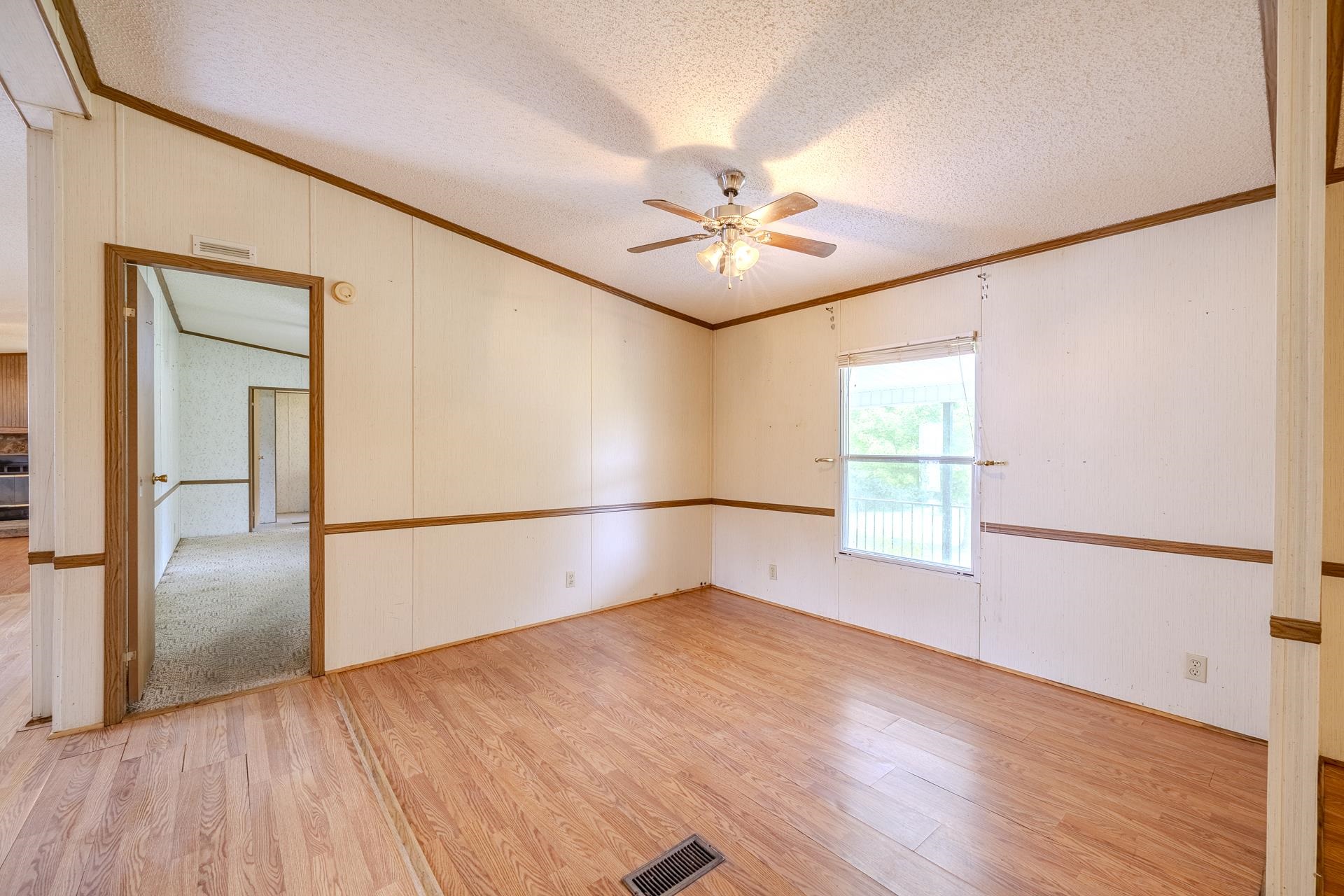859 Old Morris Chapel Road Adamsville, TN 38310 - Photo 17 of 39 Spacious room featuring wood-finish flooring, white panel walls with wood trim, a ceiling fan with integrated lighting, and a large window providing ambient light