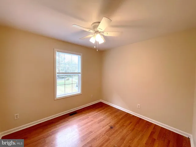 an empty room with wooden floor fan and windows
