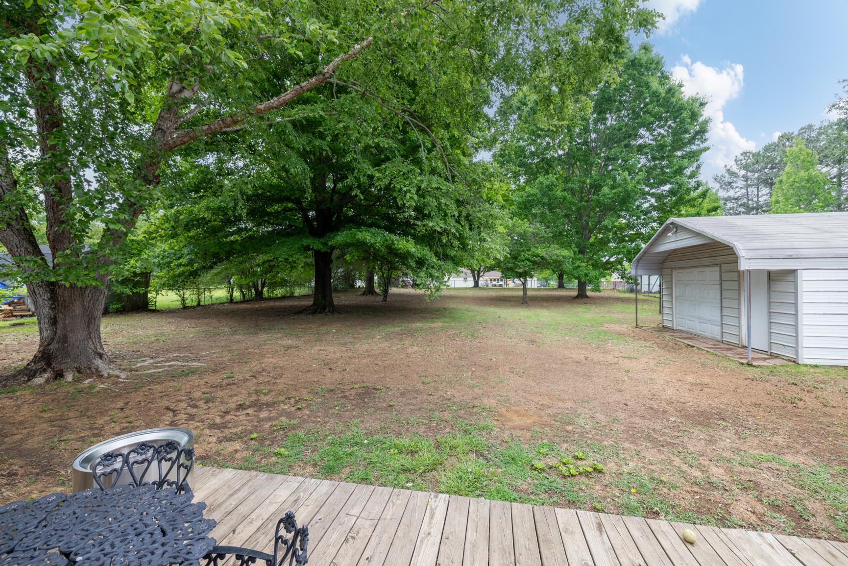 586 Beaver Road Munford, TN 38058 - Photo 18 of 21 Expansive backyard featuring mature trees, a wooden deck, and a detached white storage structure with a covered entrance