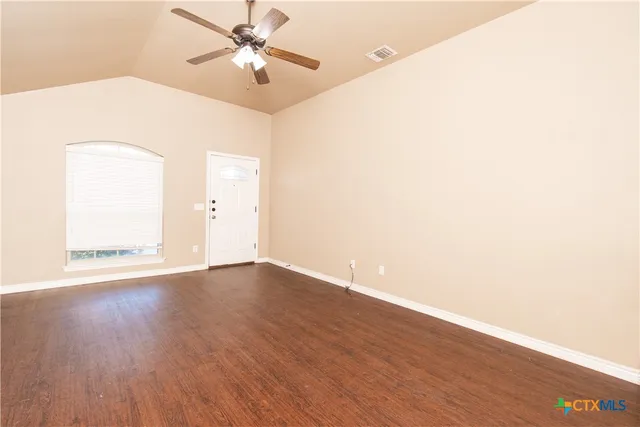 a view of an empty room with wooden floor and a ceiling fan