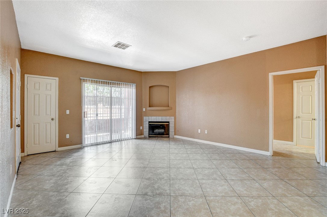 Unfurnished living room featuring a tiled fireplace and light tile patterned floors