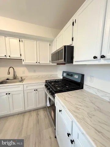 a kitchen with stainless steel appliances a sink dishwasher stove refrigerator and white cabinets with wooden floor