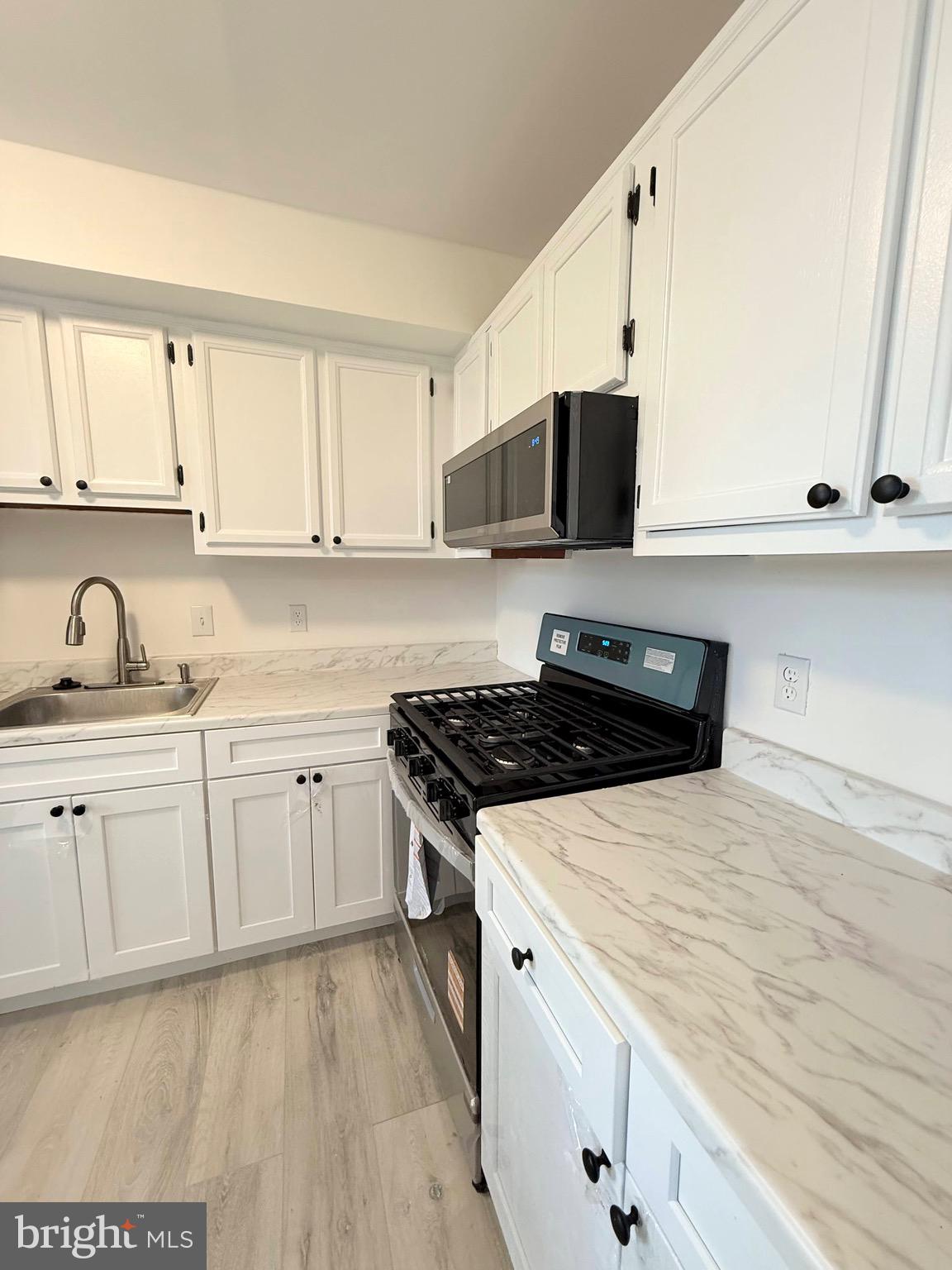 730 Quince Orchard Boulevard, Unit 730101 Gaithersburg, MD 20878 - Photo 10 of 47 a kitchen with stainless steel appliances a sink dishwasher stove refrigerator and white cabinets with wooden floor