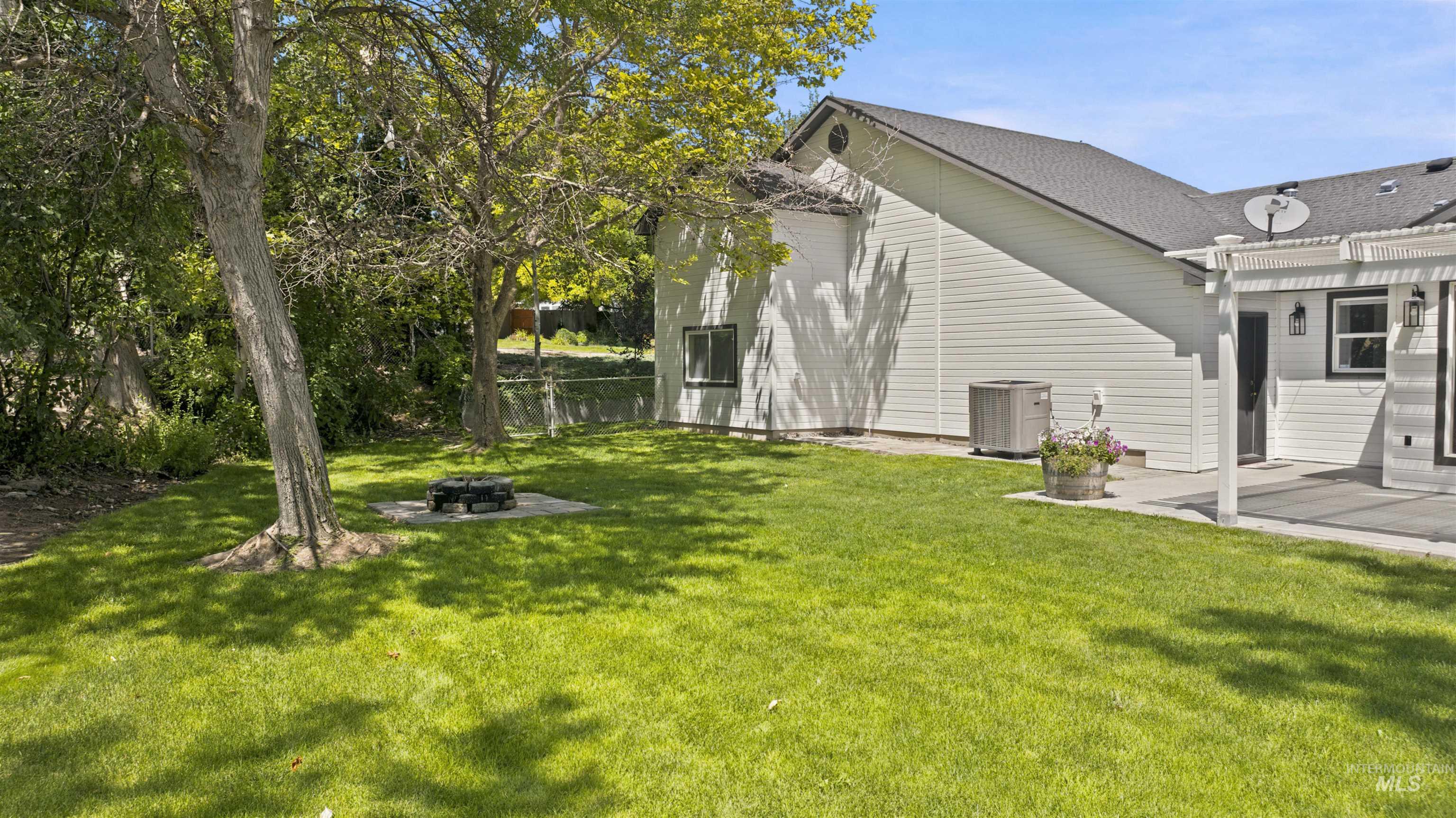 24864 Coventry Drive Caldwell, ID 83607 - Photo 49 of 49 Spacious backyard featuring a manicured lawn, established shade trees, a fire pit area with a paver base, a concrete patio, and an attached pergola