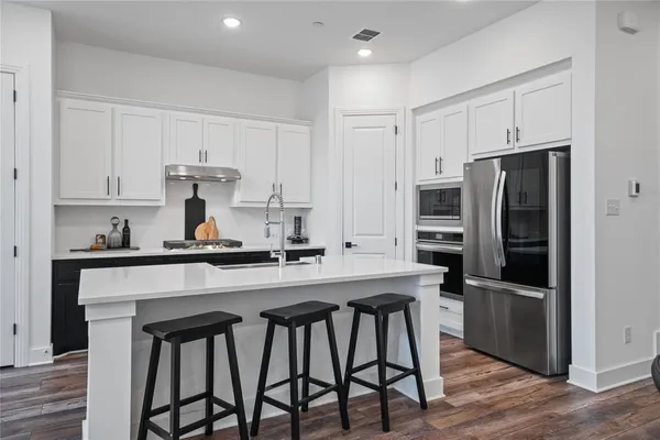 a kitchen with stainless steel appliances a sink a stove a refrigerator cabinets and wooden floor